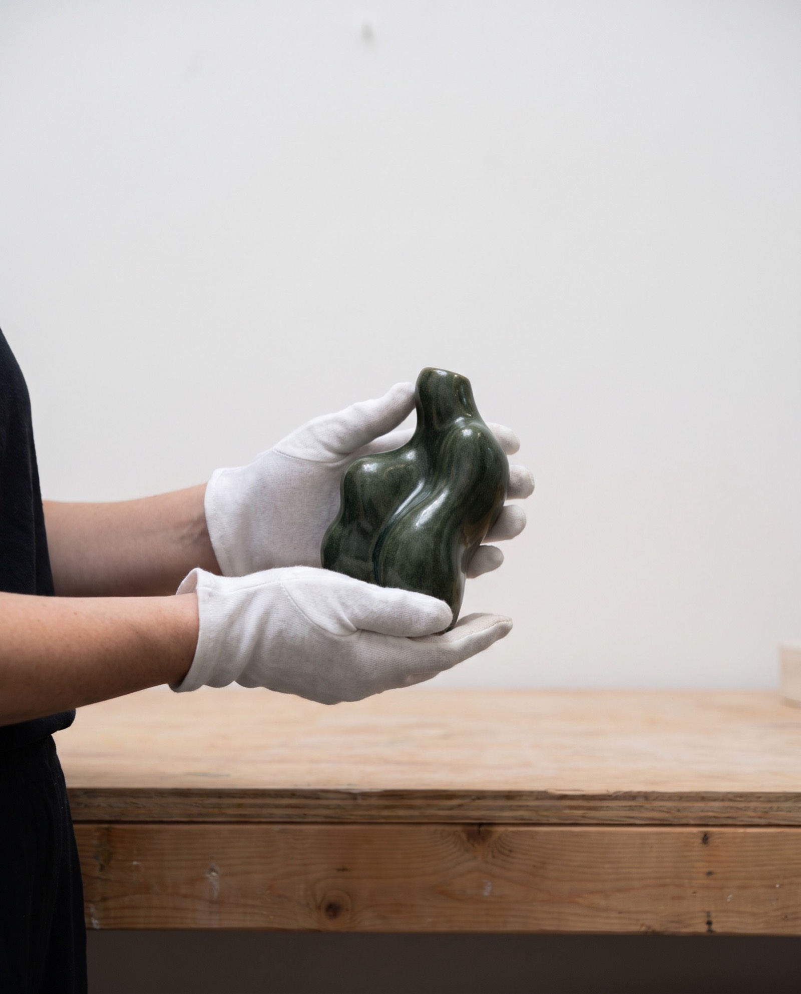 Mains gantées tenant une petite sculpture en grès vert
